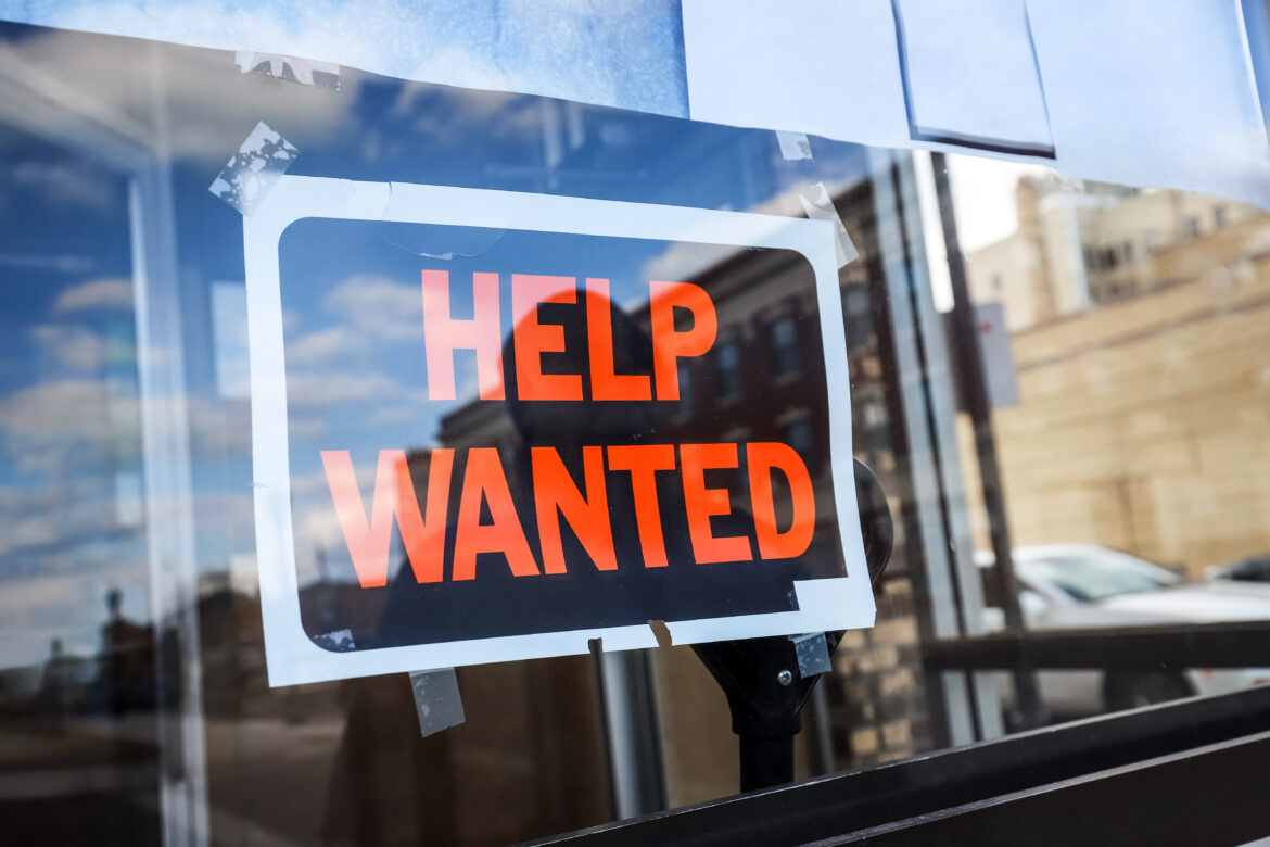 Reflection of a man looking at a help wanted sign in a business window economy concept